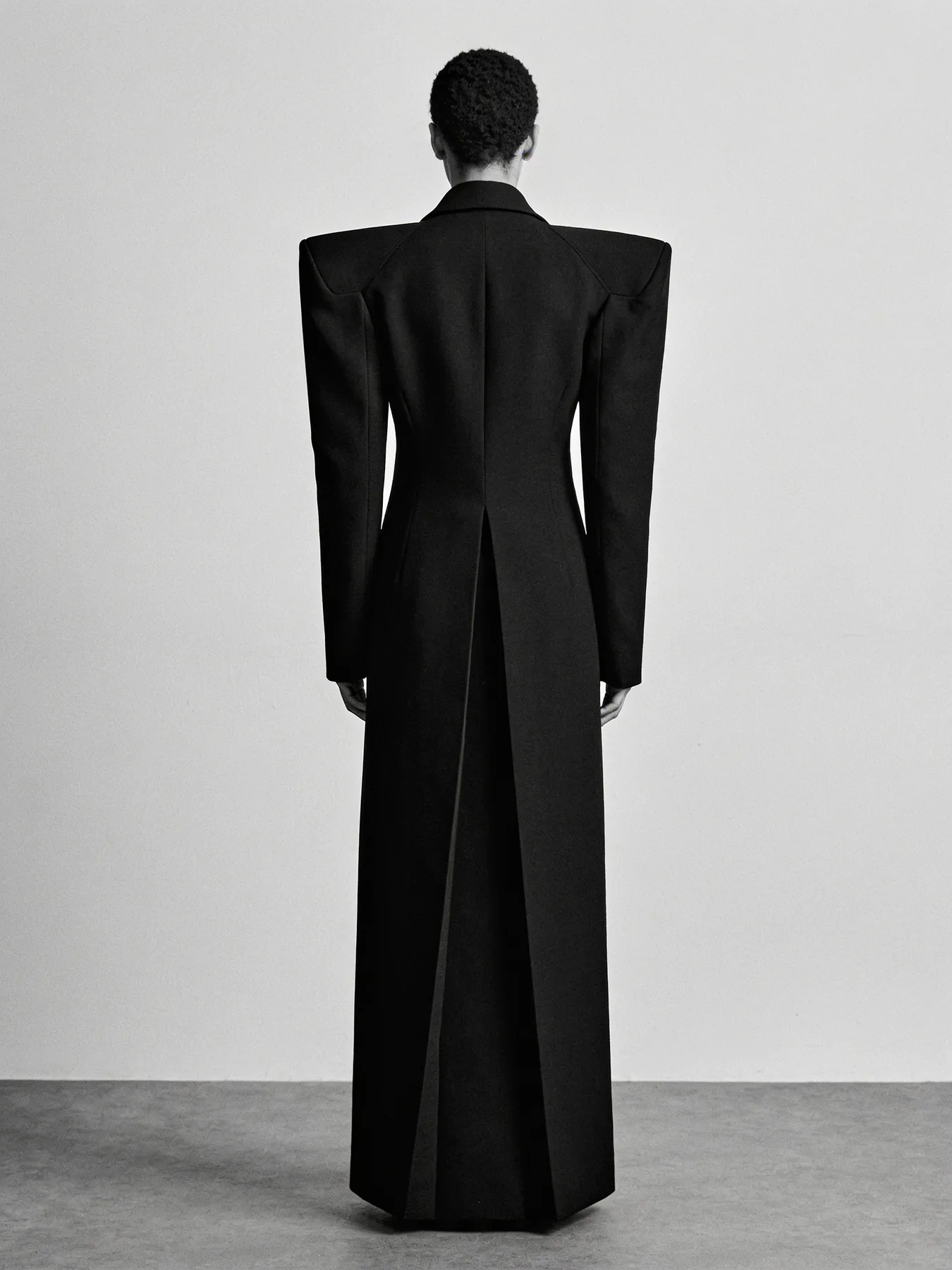 Long black column coat seen from behind with inverted box pleat